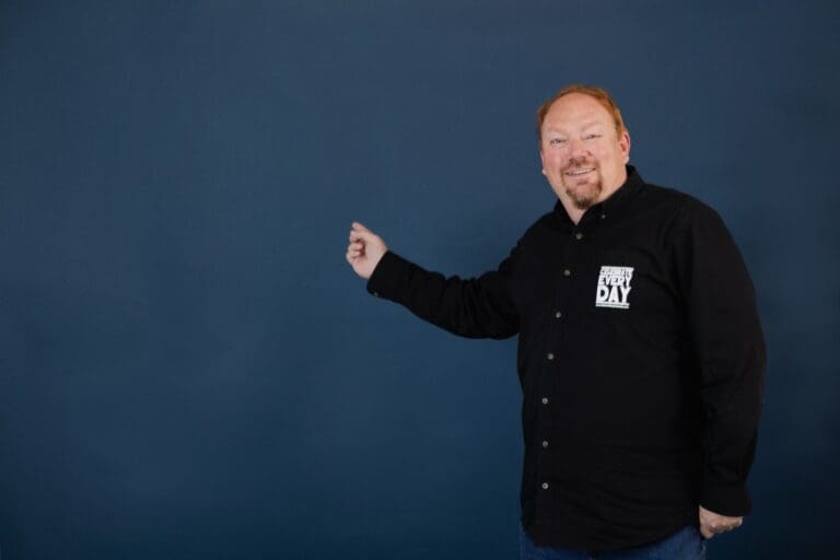 Marlo Anderson pointing upward against a blue wall